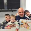 Un padre seduto sul divano e leggendo il libro per famiglie con mamma, papà e 3 bambini
