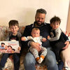 Un papà seduto sul divano e leggendo il libro di Urrà Eroi, un regalo perfetto per ogni occasione.