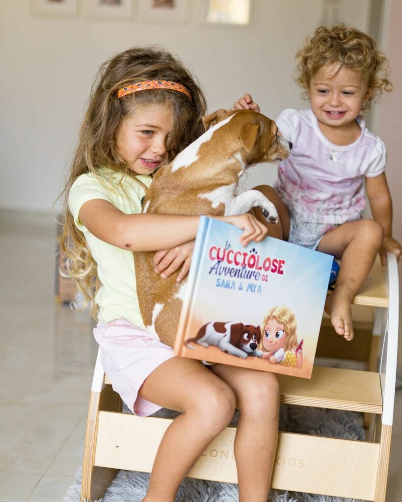 Sorelle che tengono in braccio il loro cane e libro personalizzato per loro e per il loro cane. 