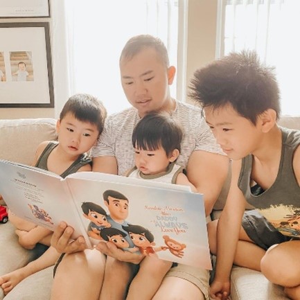 Un padre legge il libro personalizzato Papà vi amerà per sempre con i suoi tre figli seduti sul divano a casa.