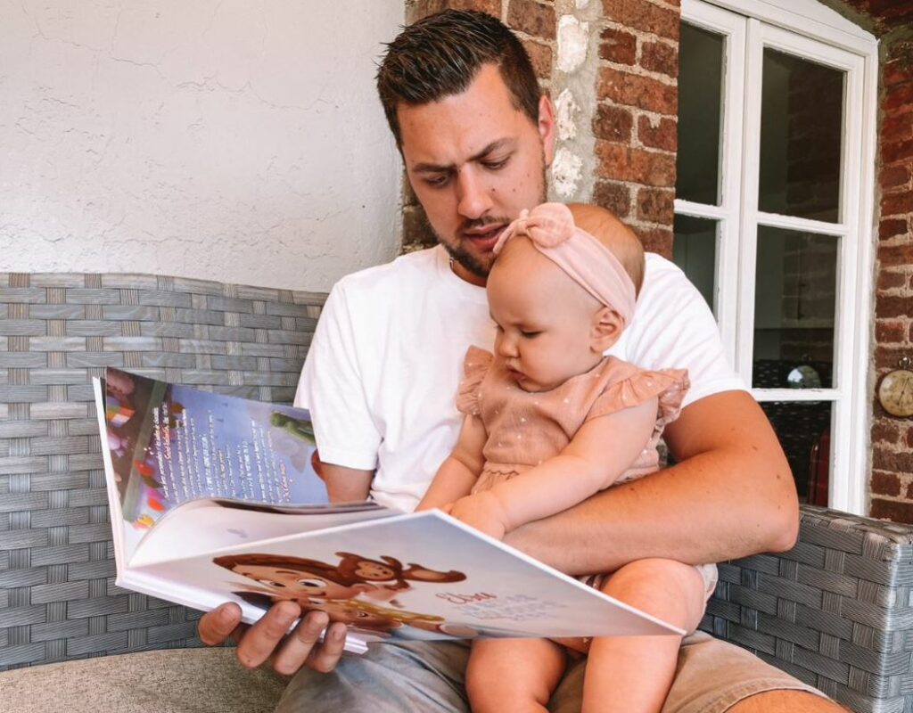Un padre è seduto con la sua bambina su un divano a leggere il loro libro personalizzato.