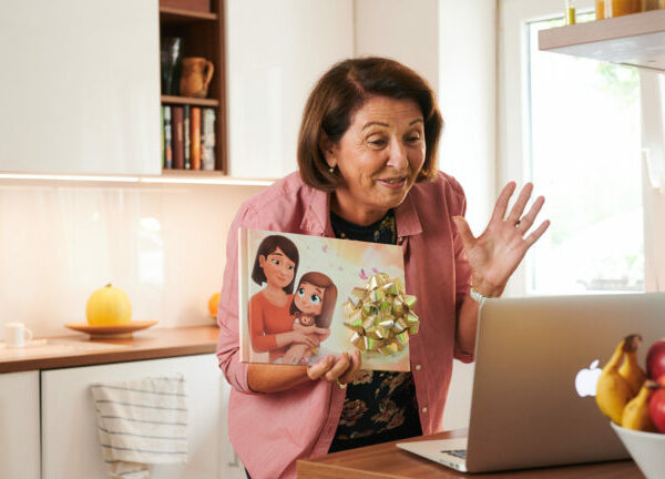 Una nonna mostra il suo libro personalizzato tramite lo zoom del computer portatile mentre si trova in cucina.