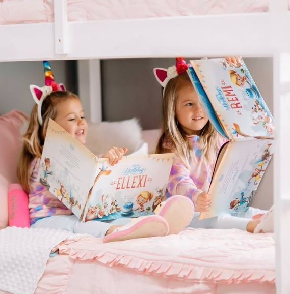 due bambine sedute sul letto che si mostrano a vicenda il loro libro di compleanno personalizzato.