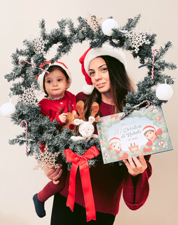Una mamma e un bambino che presentano il libro personalizzato 10 desideri per il Natale con cappelli e ghirlande natalizie.