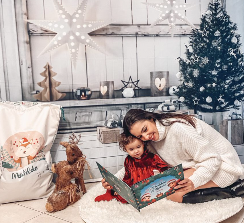 una mamma e un bambino guardano il loro libro personalizzato di Urrà Eroi in una casa decorata a Natale